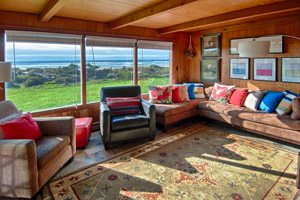 Living room with colorful couch cushions, area rug and big windows overlooking the ocean