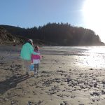 Woman and child walk along rocky beach at low tide