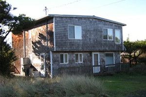Two-story wooden-shingled building with a pine tree next to it