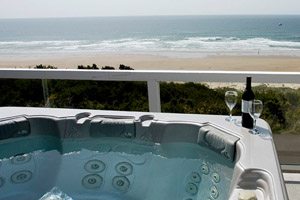 Hot tub with wine bottle and glasses on the side, set up on balcony next to the beach